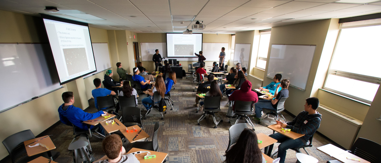 classroom with students and instructors viewing class materials on a projector screen